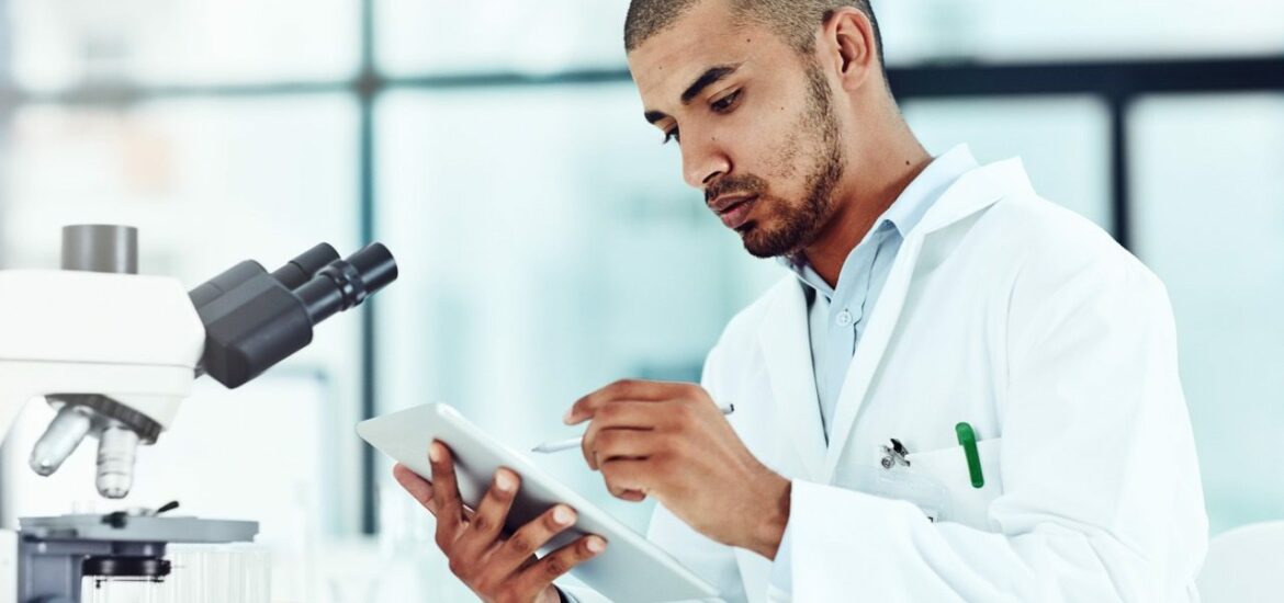 Serious male scientist working on a tablet reviewing an online phd publication in a lab. Laboratory worker updating health data for a science journal. Medical professional document clinical trial.